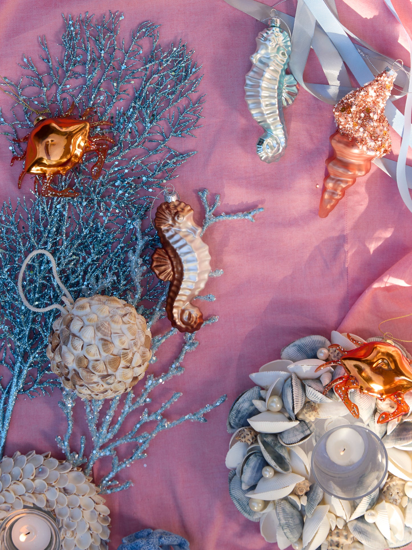 Holly & Ivy coastal Christmas flatlay with seahorse ornaments, coral décor, shells and candlelight.